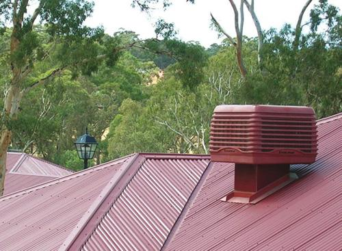Evaporative cooling unit installed on a red tin roof surrounded by gum trees