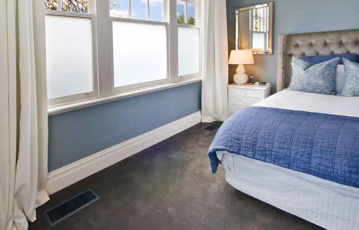 Blue and white bedroom with a gas ducted heating floor vent set into the carpet