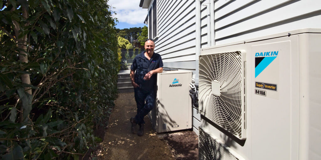 Technician standing beside outdoor Daikin and ActronAir air conditioning units.